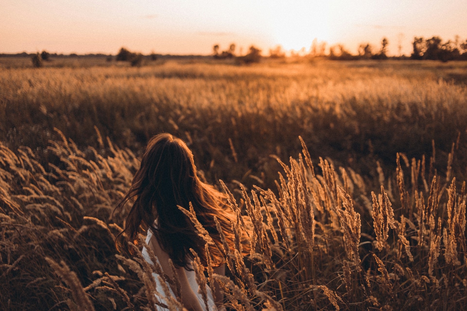 Frau geht bei Sonnenuntergang durch ein Kornfeld
