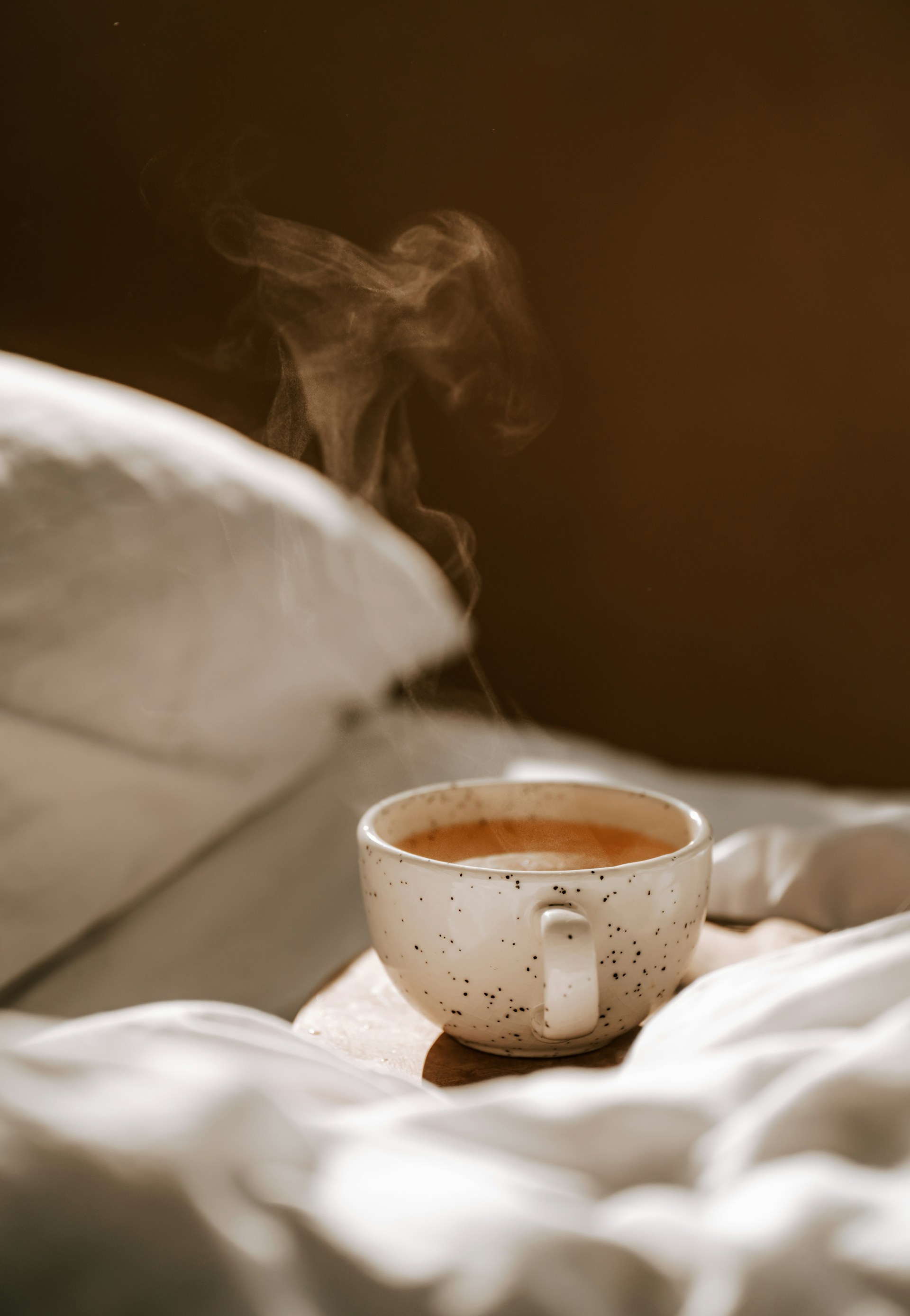 Dampfende Tasse Kaffee auf weißer Bettwäsche