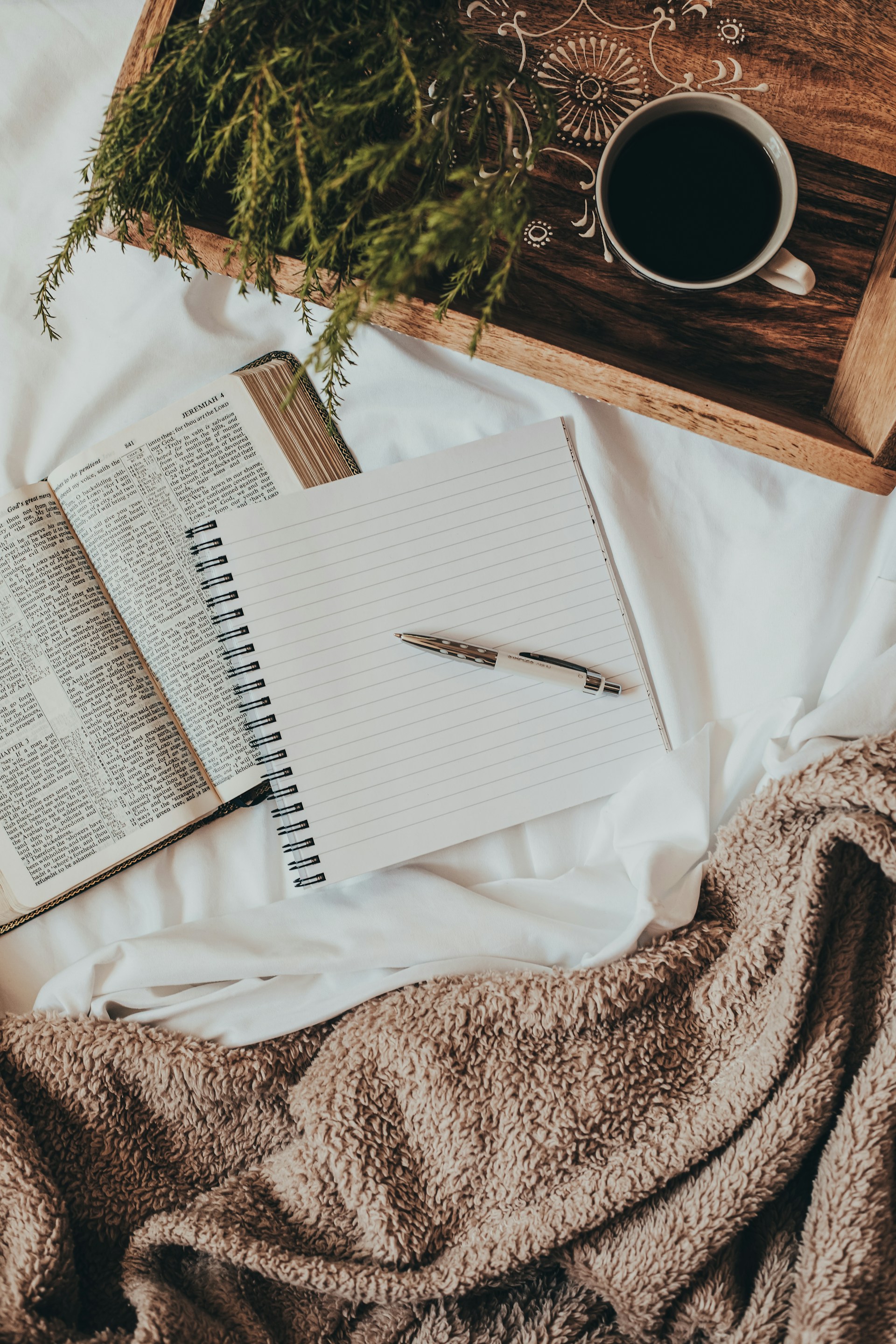 Aufgeschlagenes Notizbuch mit Stift auf einem Bett, daneben Kaffee auf einem Holztablett