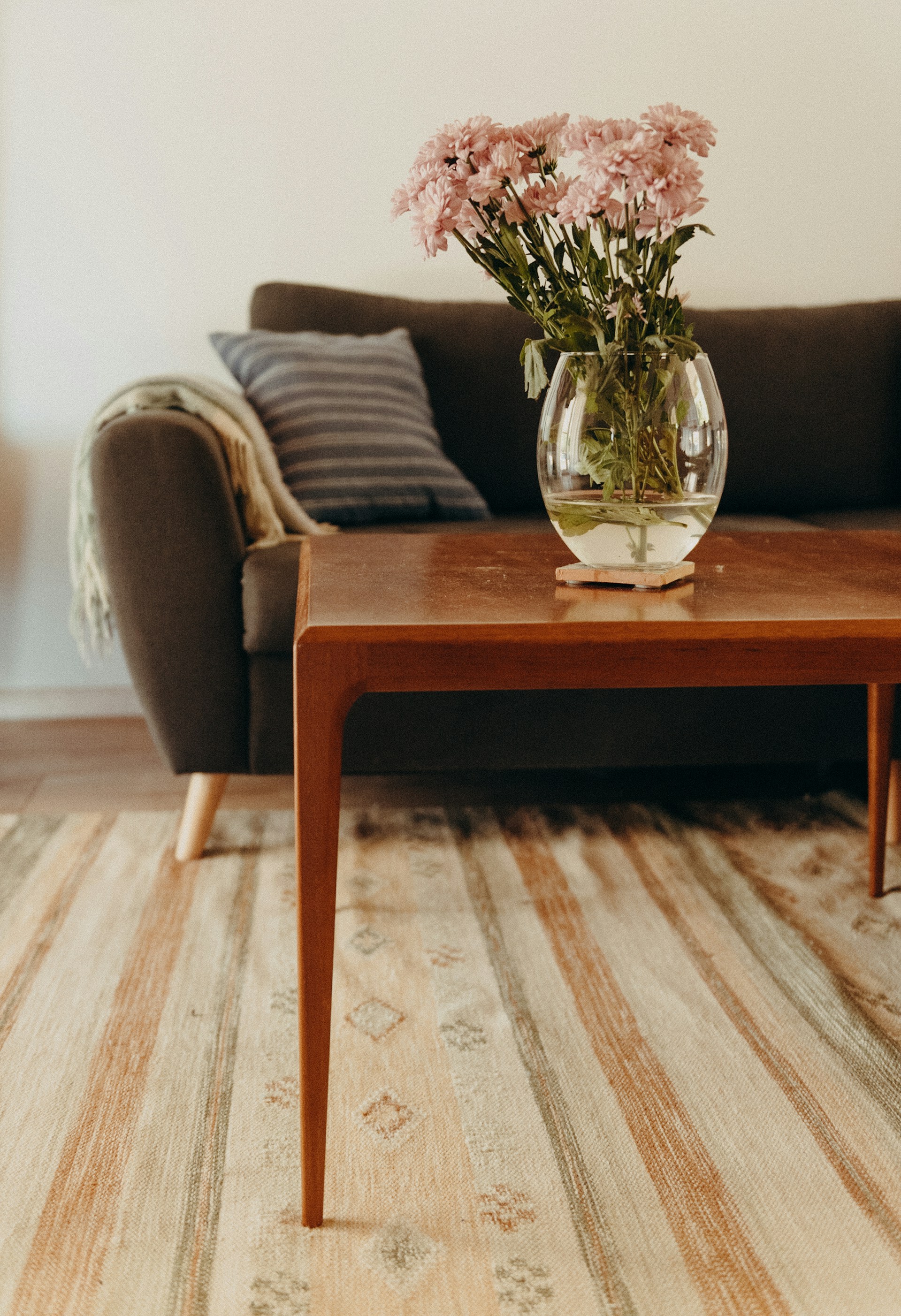 Wohnzimmer mit Holztisch, einer Vase mit rosa Blumen und einem Sofa