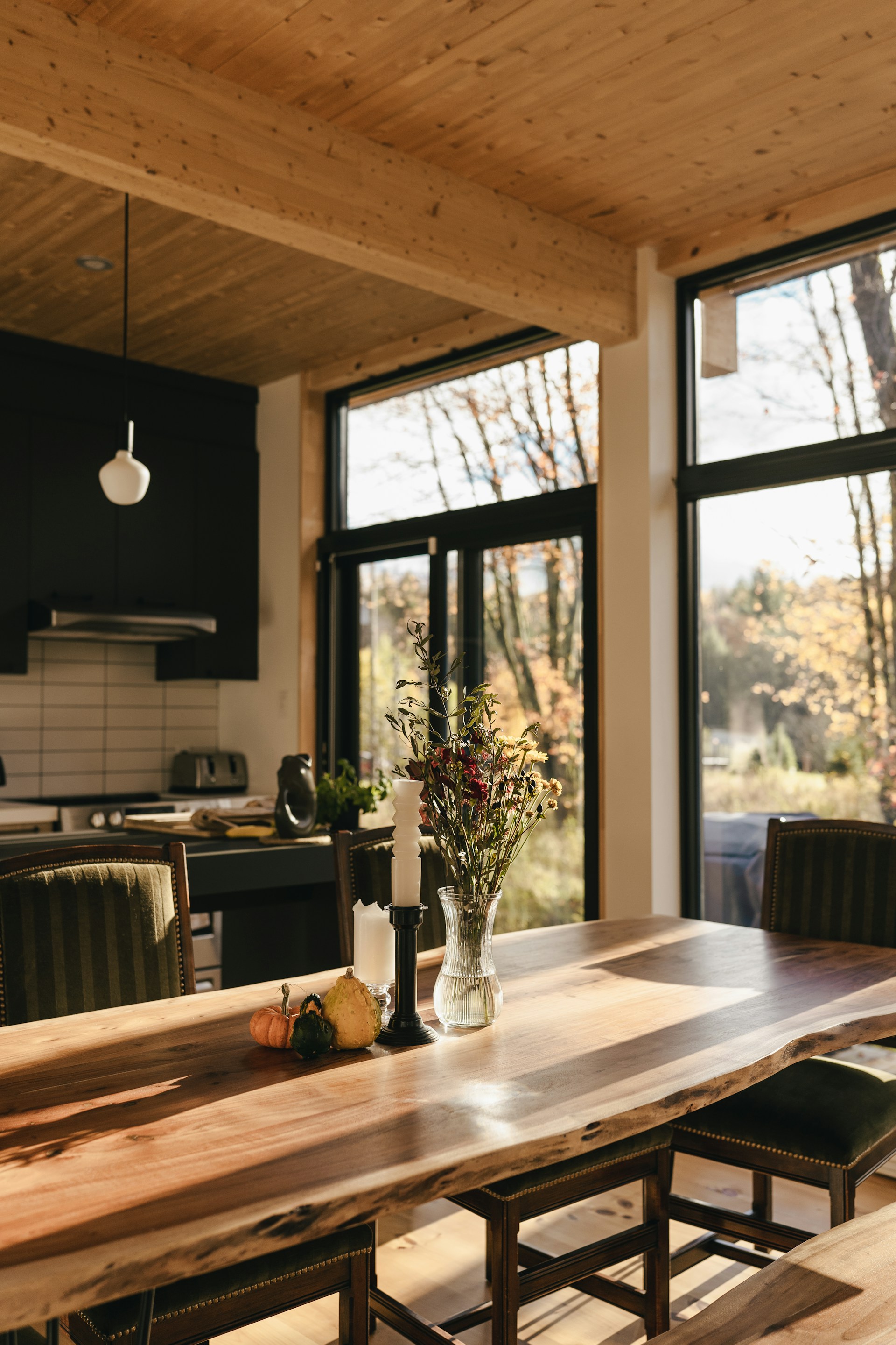 Holztisch mit Blumenvase in einem hellen Esszimmer mit Blick in den herbstlichen Wald