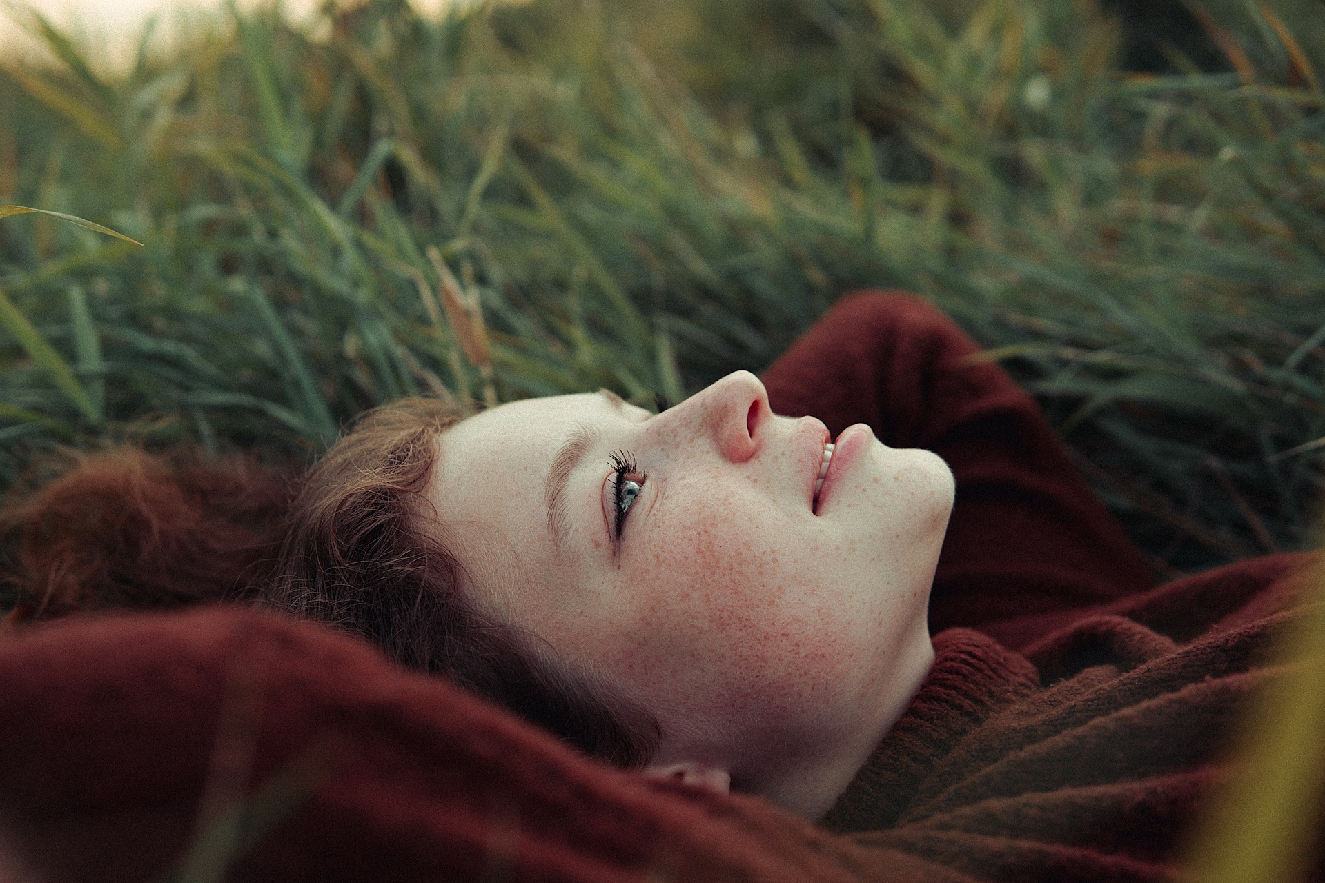 Frau liegt nachdenklich im Gras, das Gesicht dem Himmel zugewandt