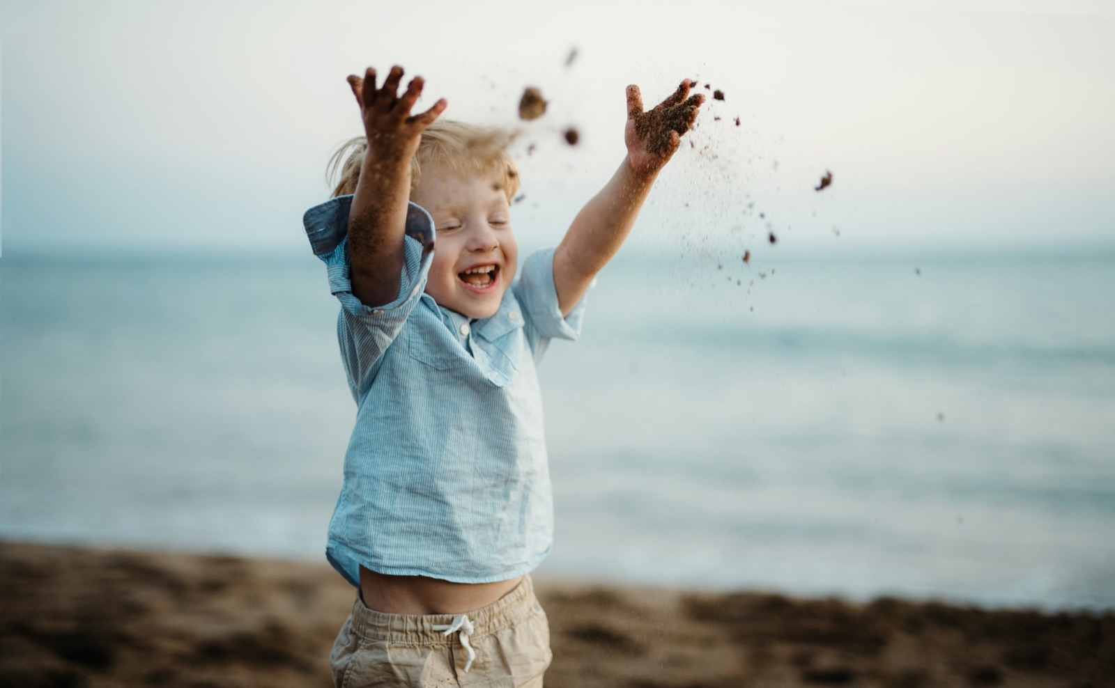 Lachendes Kind am Strand wirft fröhlich Sand in die Luft