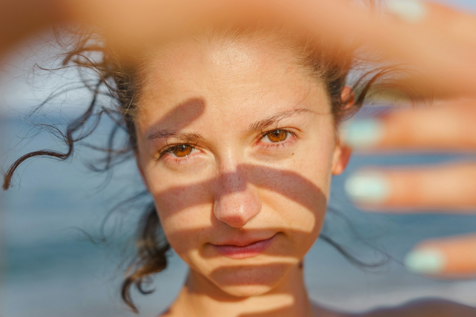 Frau hält die Hand gegen die Sonne, Lichtstreifen und Schatten fallen über ihr Gesicht