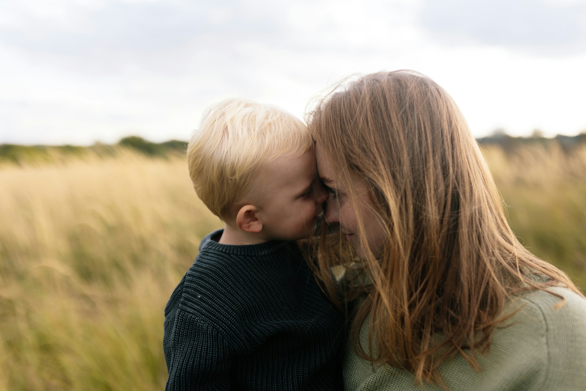 Mutter und kleiner Sohn stehen Stirn an Stirn auf einem Feld, ein ruhiger Moment der Verbundenheit