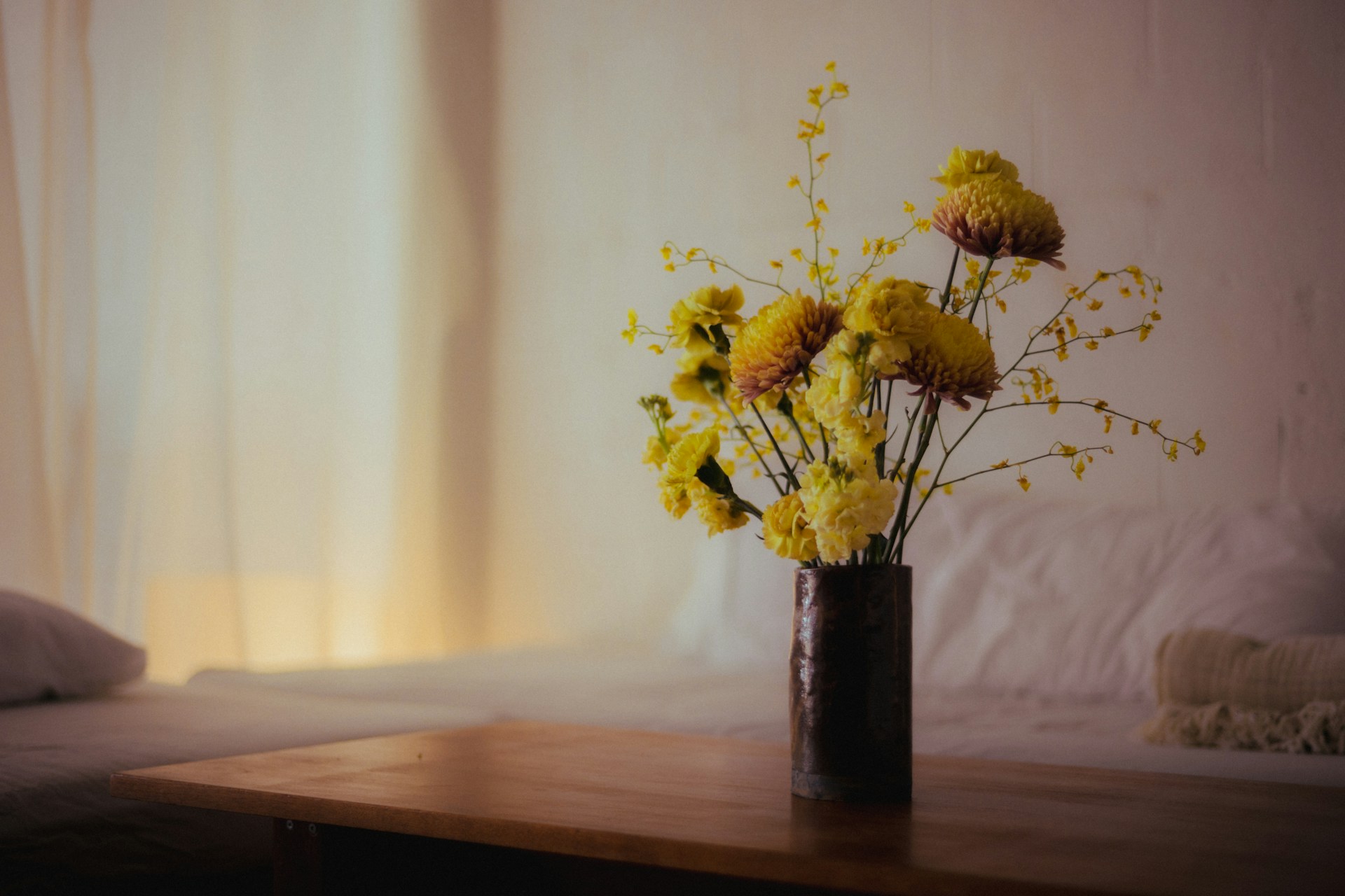 Schlichte Vase mit gelben Blumen auf einem Holztisch im warmen Tageslicht