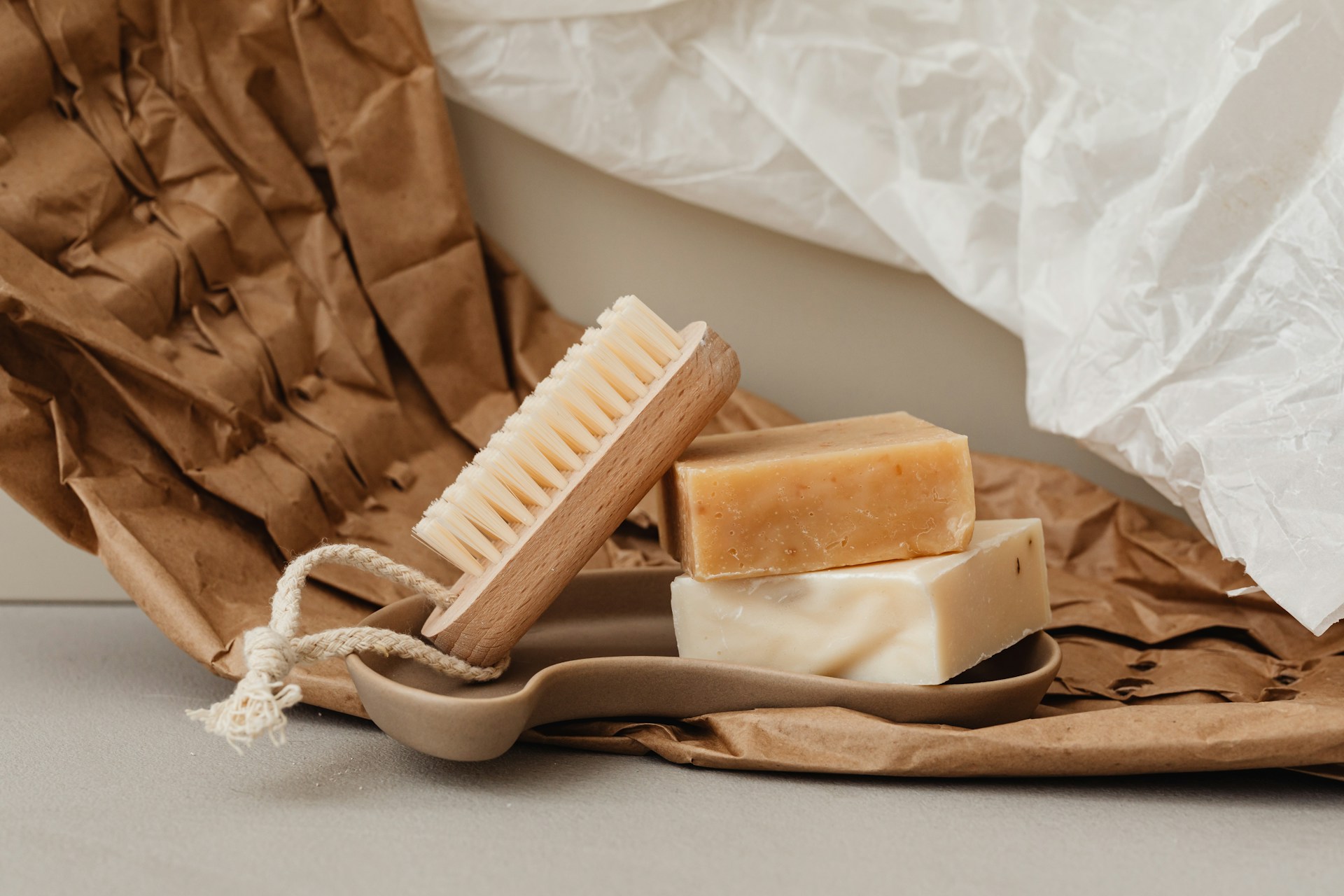 Zwei Stück Naturseife und eine Holzbürste auf einer Seifenschale, verpackt in Kraftpapier