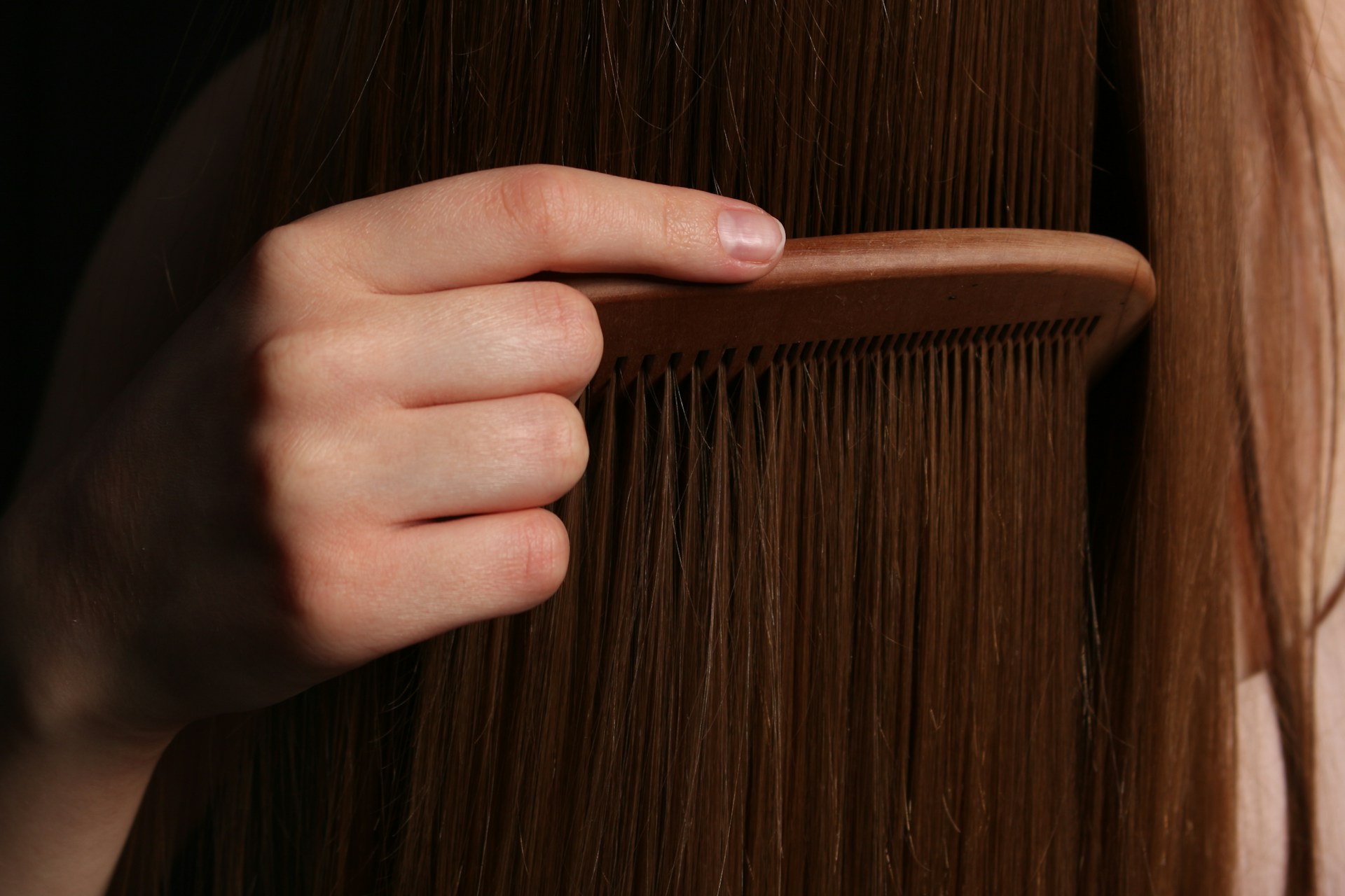 Nahaufnahme einer Hand, die langes Haar mit einem Holzkamm kämmt