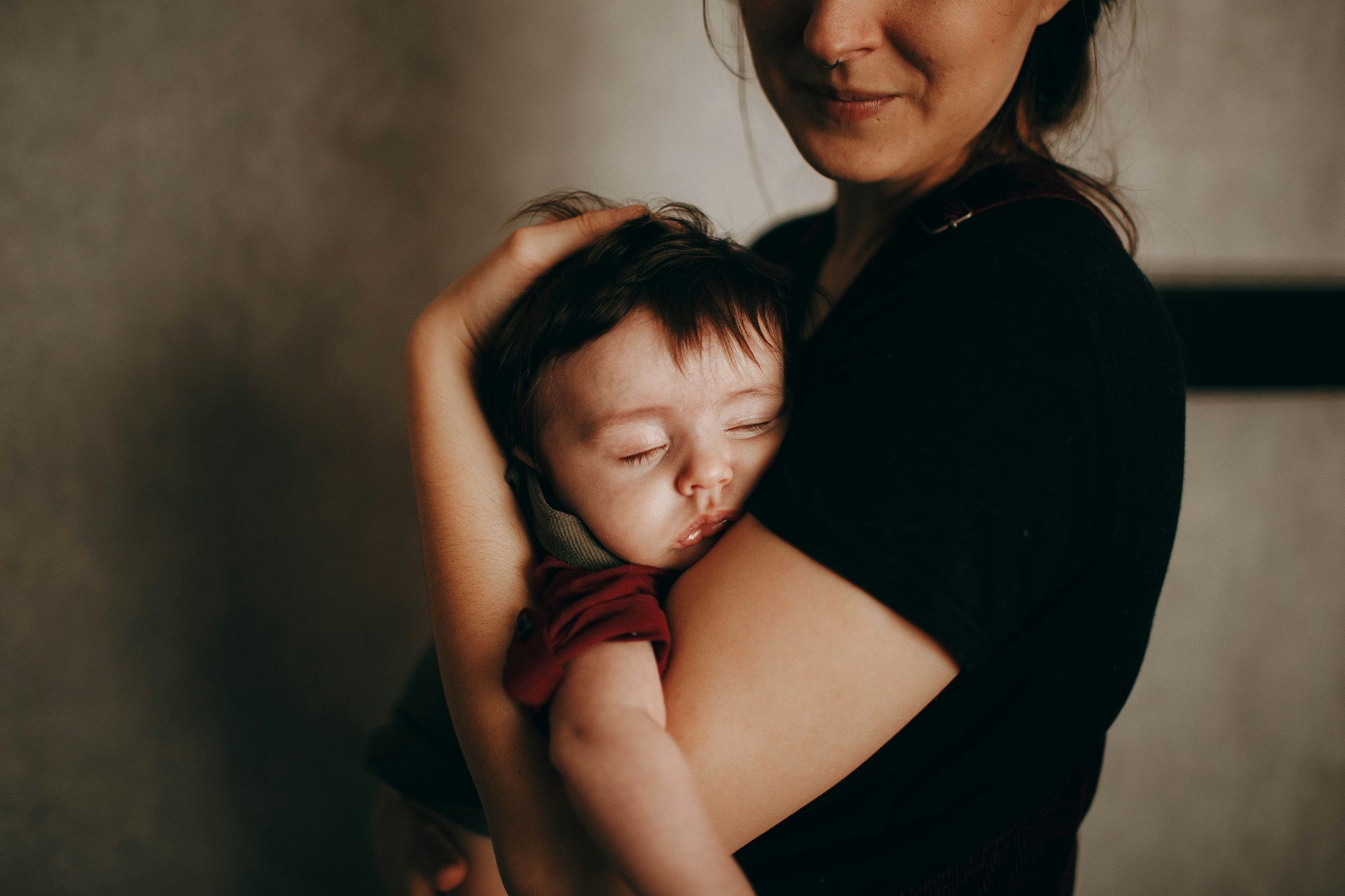Mutter hält ihr schlafendes Baby ganz nah, ihr Gesicht ist oben vom Bildrand abgeschnitten, nur Nase und Lächeln sichtbar