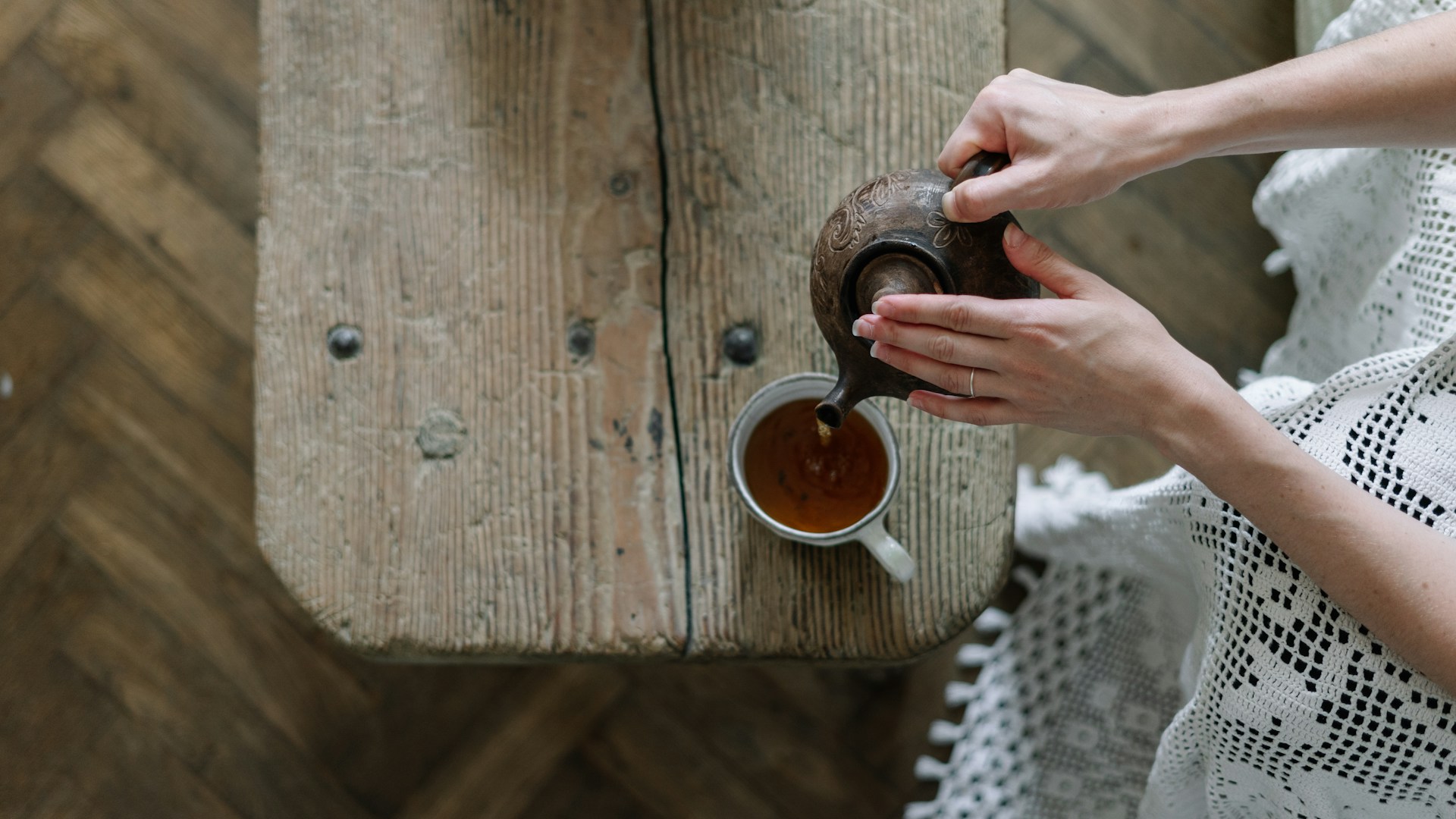 Draufsicht: Hände gießen Tee aus einer Kanne in eine Tasse auf einem rustikalen Holztisch