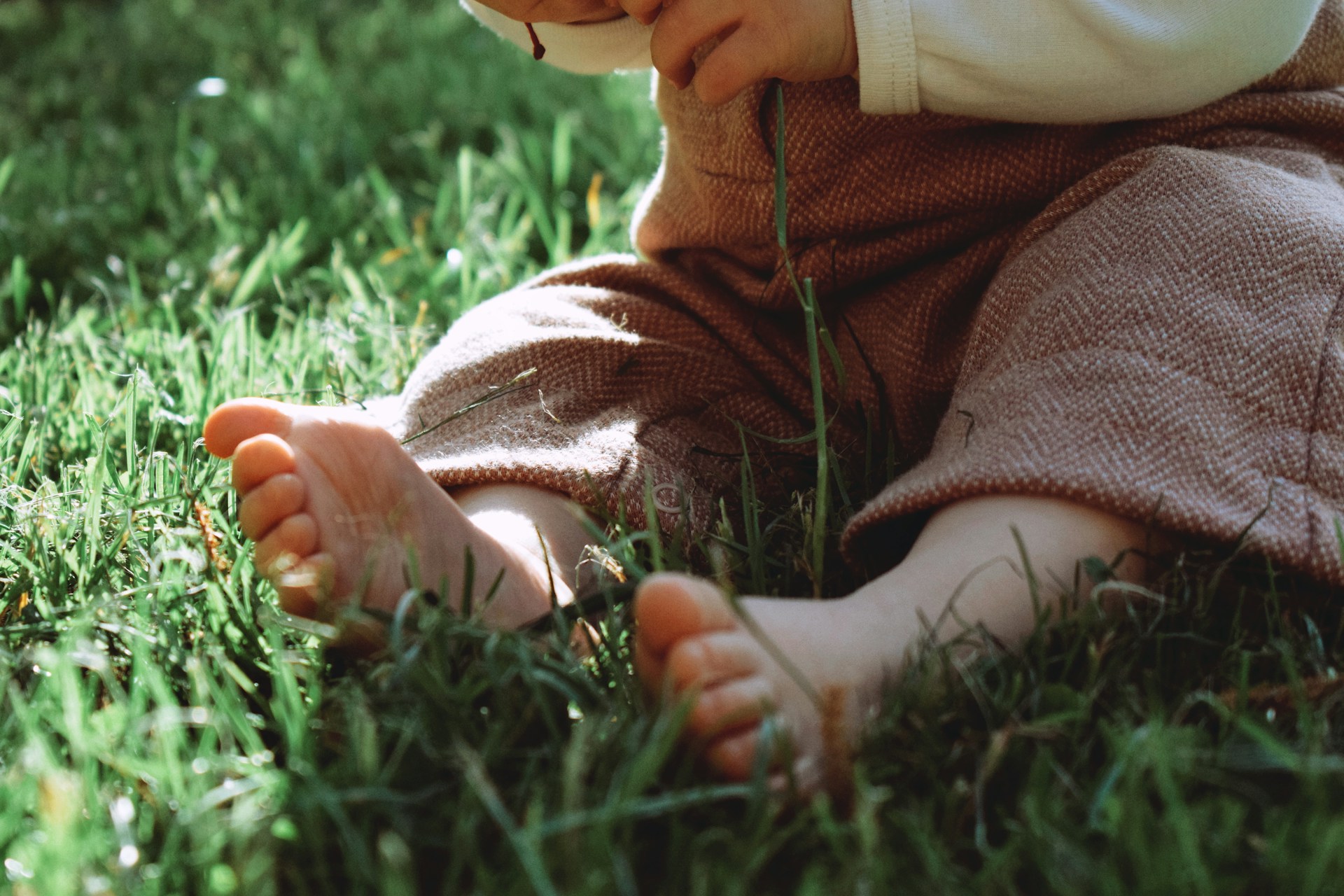 Kleines Kind sitzt barfuss im Gras